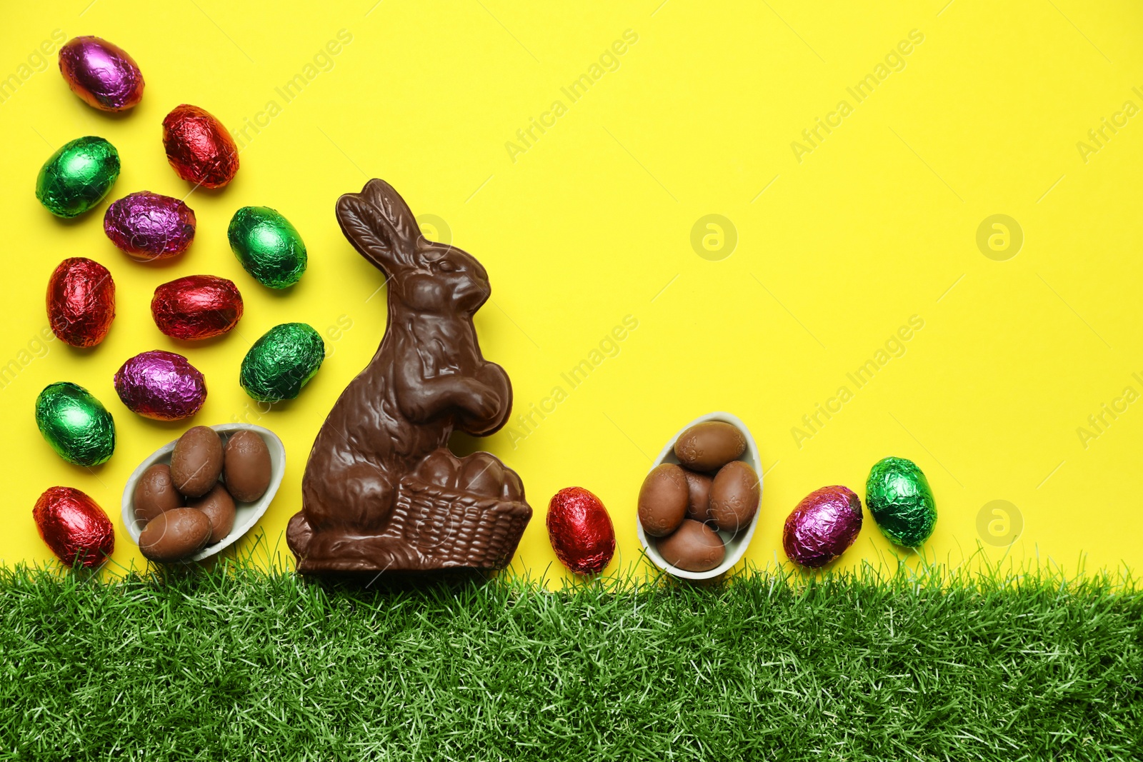 Photo of Chocolate Easter bunny and eggs with green grass on yellow background. Space for text