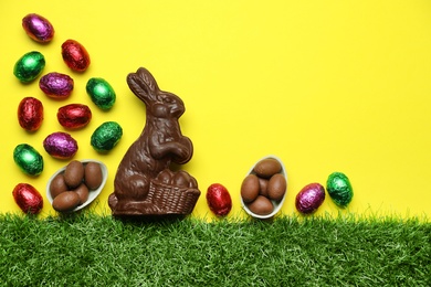 Chocolate Easter bunny and eggs with green grass on yellow background. Space for text