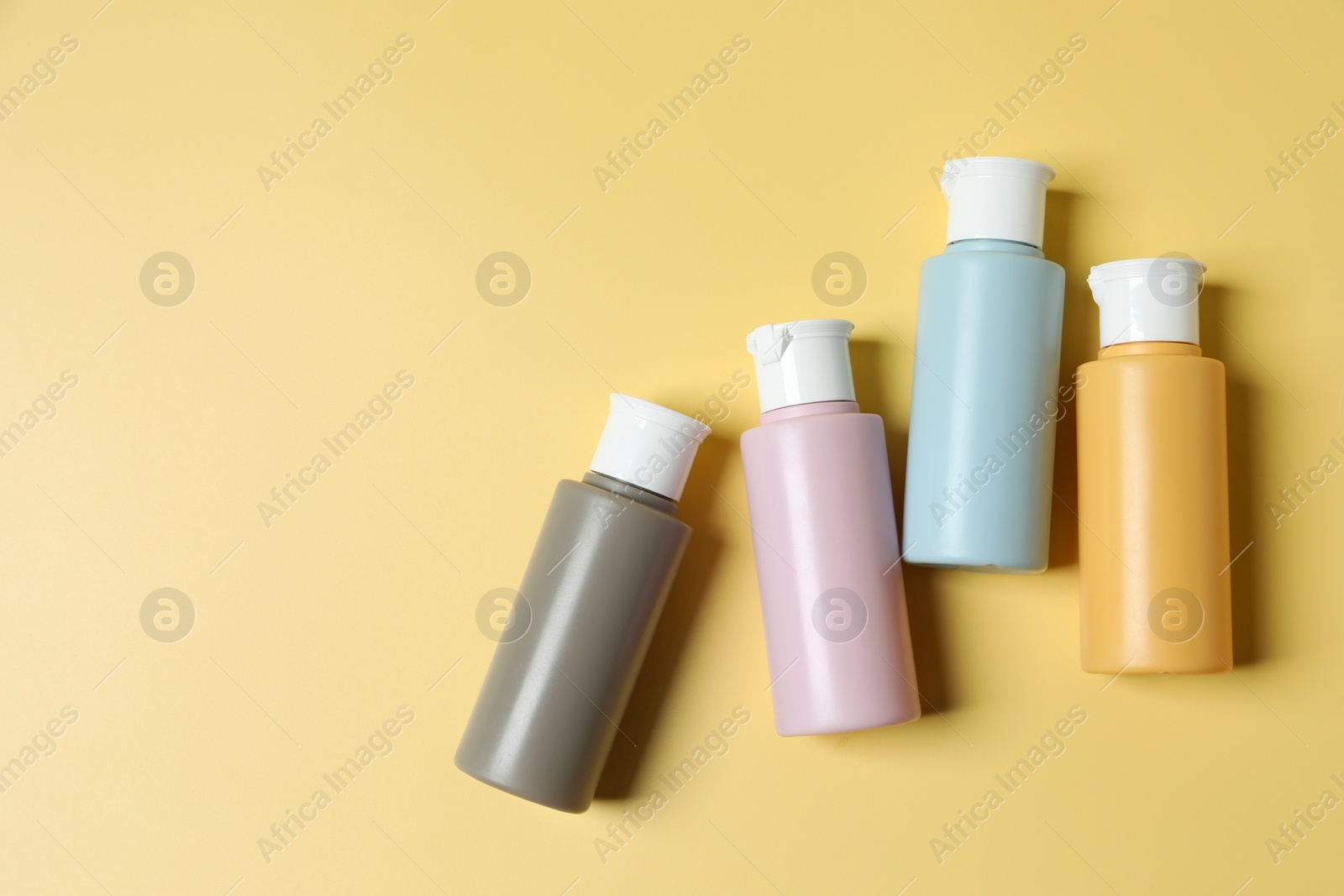 Photo of Cosmetic travel kit. Small containers of personal care products on yellow background, flat lay. Space for text