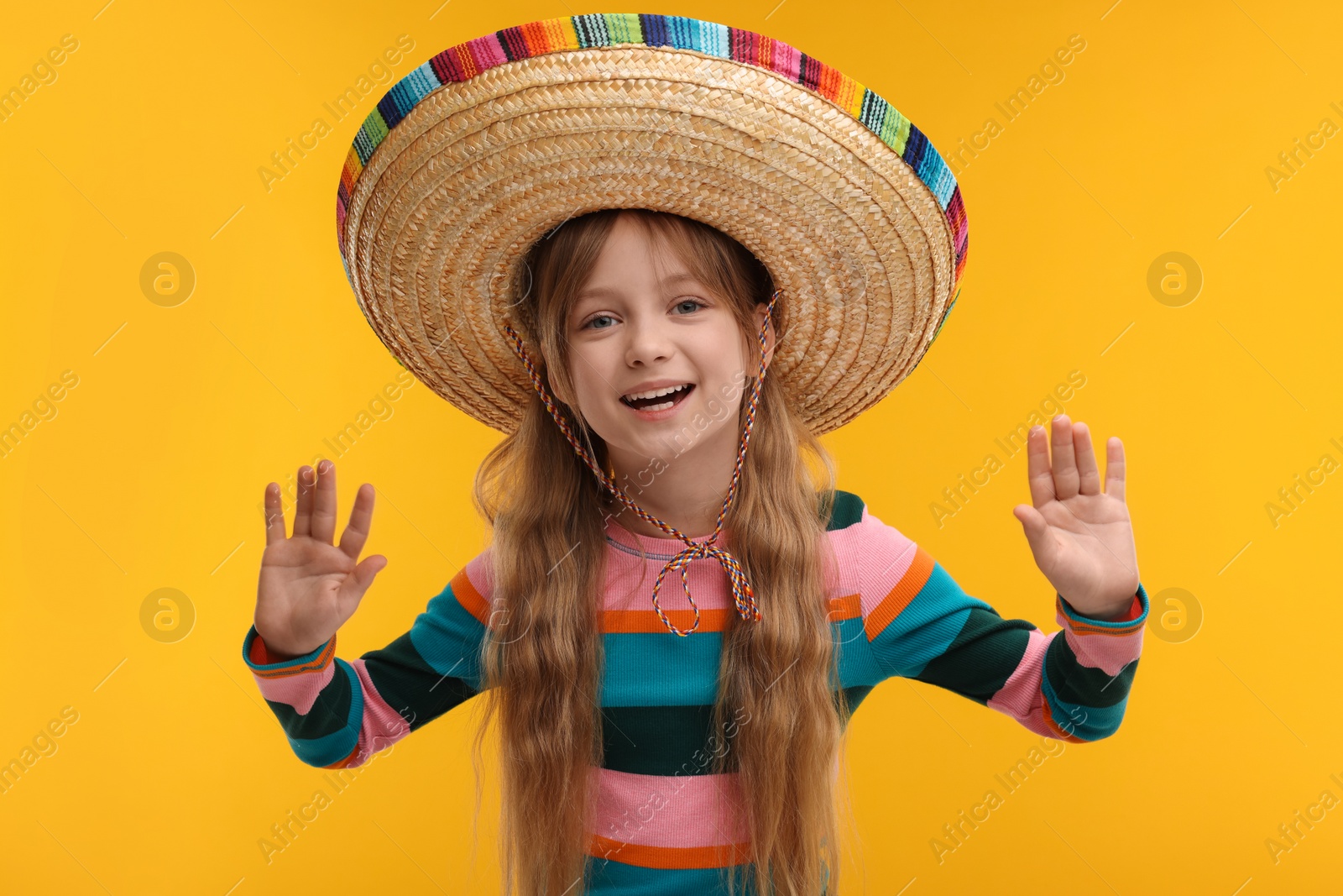 Photo of Cute girl in Mexican sombrero hat on orange background