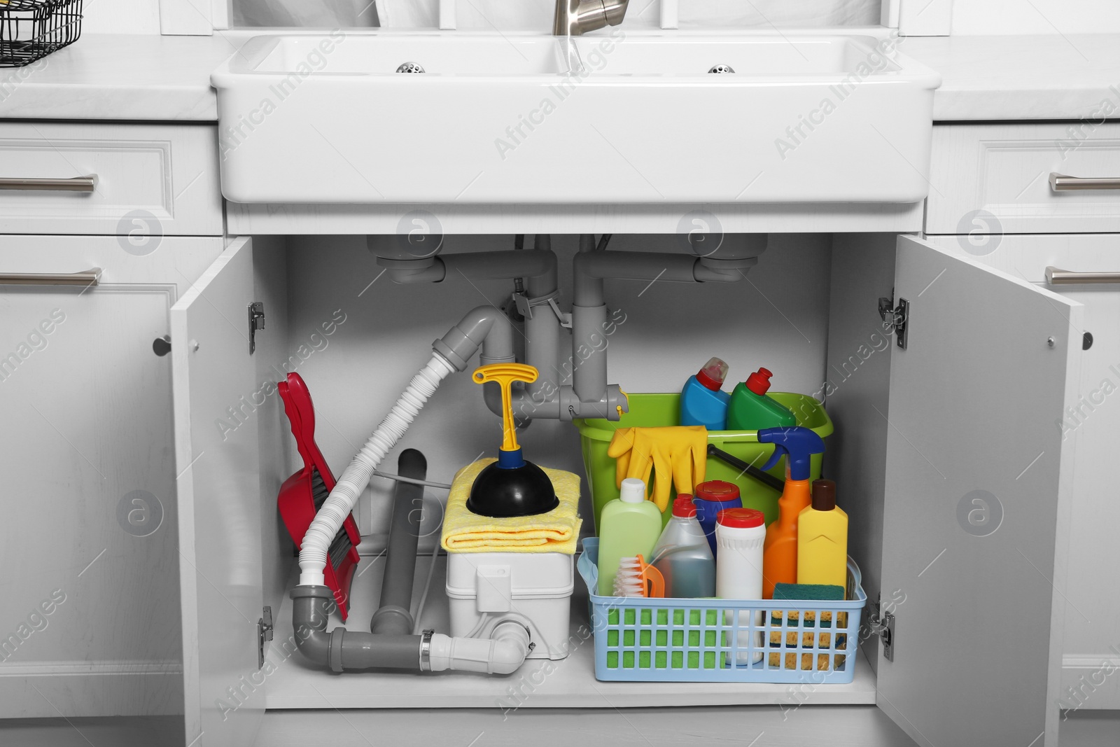 Photo of Open under sink cabinet with different cleaning supplies in kitchen