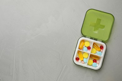 Photo of Plastic box with different pills on light grey stone table, top view. Space for text