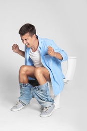 Photo of Young man suffering from diarrhea on toilet bowl against gray background