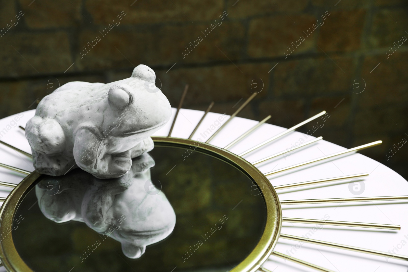 Photo of Stone frog figure with mirror on white table. Space for text