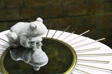 Stone frog figure with mirror on white table. Space for text