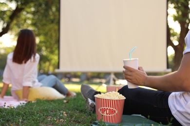 Young man with popcorn and drink watching movie in open air cinema, closeup. Space for text