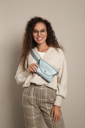 Beautiful African American woman with stylish waist bag on beige background