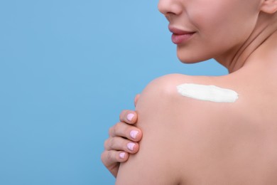 Photo of Woman with smear of body cream on her shoulder against light blue background, closeup. Space for text