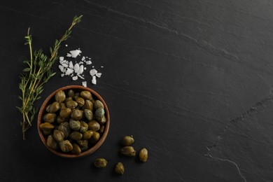 Photo of Tasty capers, salt and rosemary on black table, flat lay. Space for text