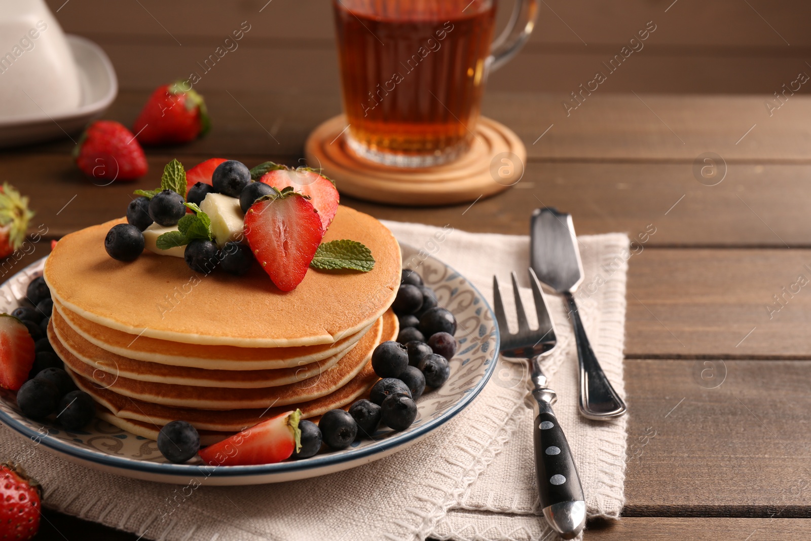 Photo of Delicious pancakes with fresh berries and butter served on wooden table, closeup. Space for text