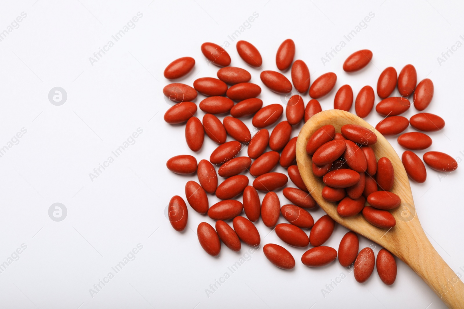 Photo of Wooden spoon and red pills on white background, flat lay with space for text. Anemia treatment