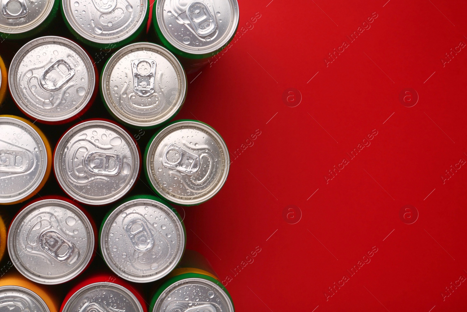 Photo of Energy drinks in wet cans on red background, top view. Space for text