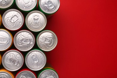Photo of Energy drinks in wet cans on red background, top view. Space for text
