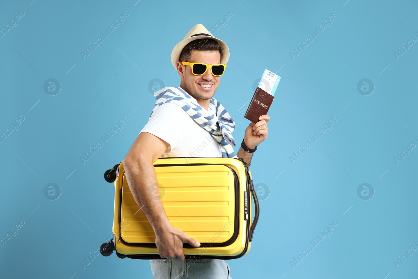 Photo of Male tourist holding passport with ticket and suitcase on turquoise background