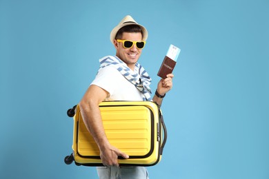 Male tourist holding passport with ticket and suitcase on turquoise background