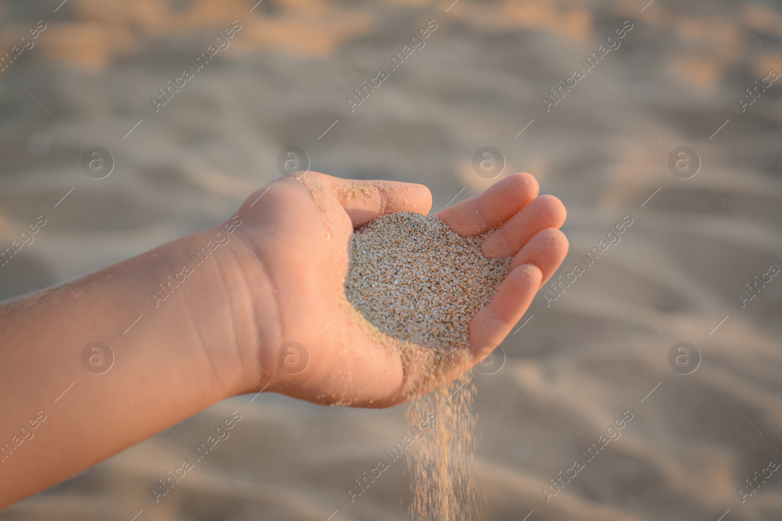 Photo of Girl pouring sand from hand outdoors, closeup. Fleeting time concept