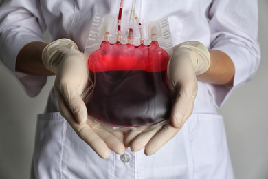 Woman holding blood for transfusion on light grey background, closeup. Donation concept