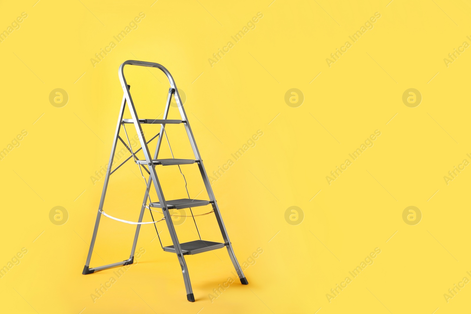 Photo of Modern metal stepladder on yellow background. Space for text