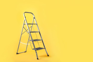 Modern metal stepladder on yellow background. Space for text