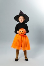 Photo of Cute little girl with pumpkin candy bucket wearing Halloween costume on grey background