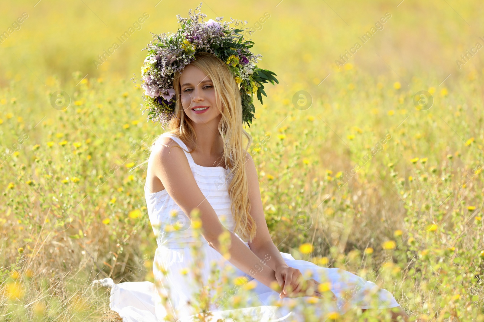 Photo of Young woman wearing wreath made of beautiful flowers in field on sunny day