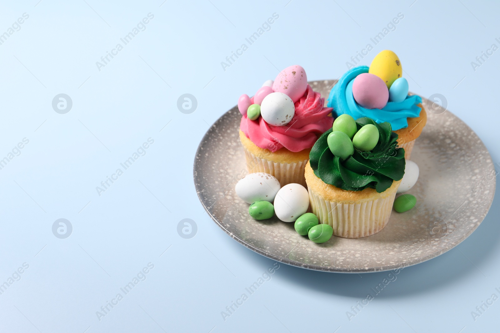 Photo of Tasty cupcakes with Easter decor on light blue background, space for text