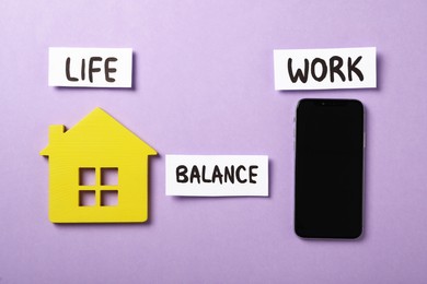 Wooden house, smartphone and words Life, Balance, Work on violet background, flat lay