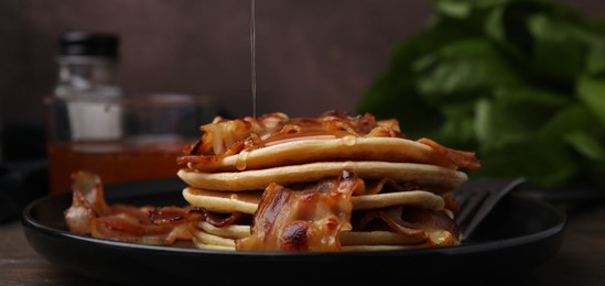Photo of Pouring maple syrup onto delicious pancakes with fried bacon on wooden table, closeup