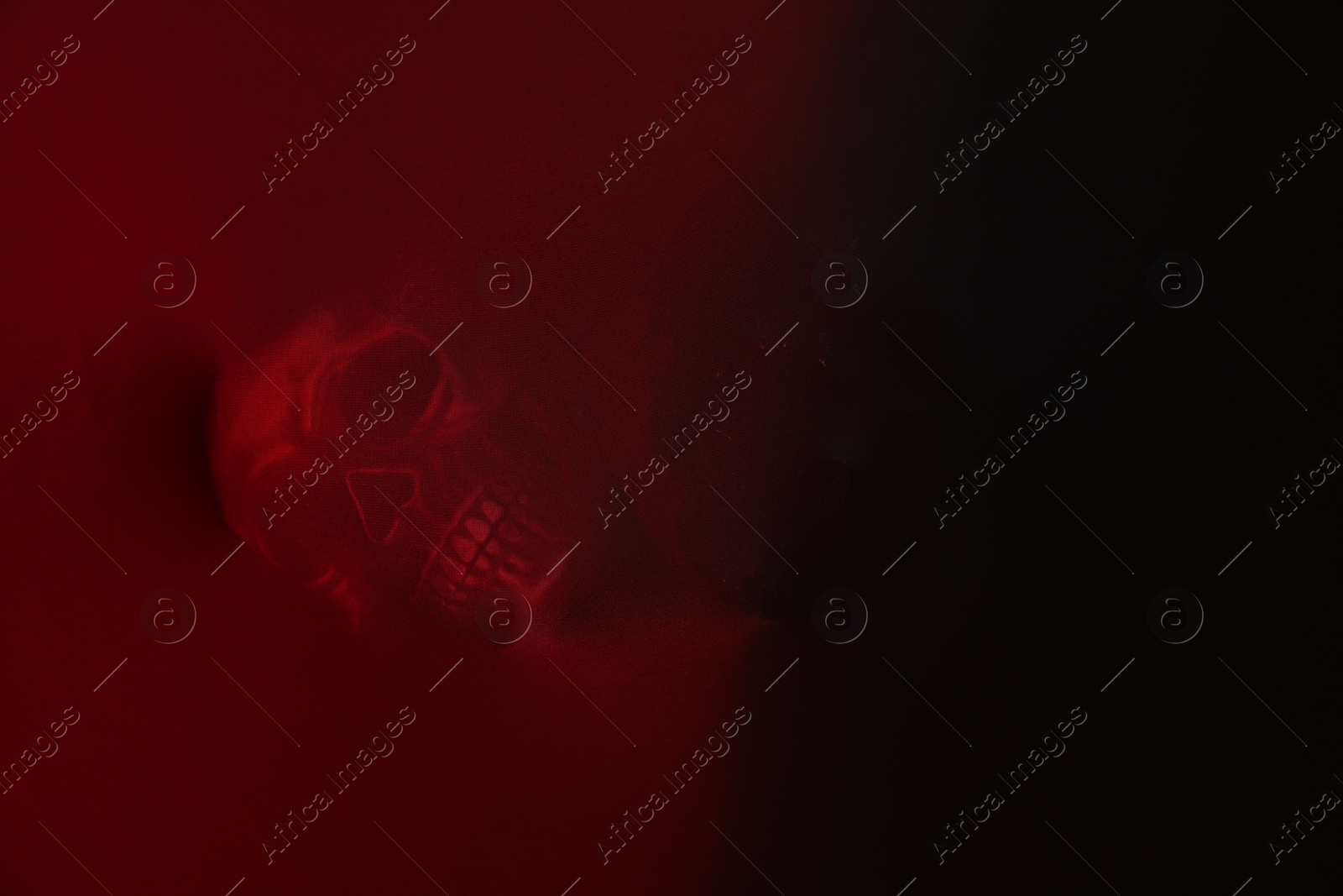 Photo of Silhouette of creepy ghost with skull behind red cloth. Space for text