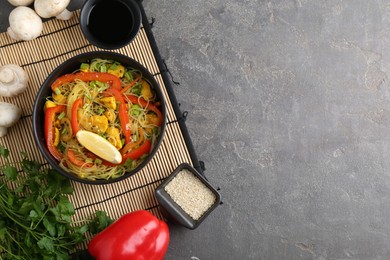 Photo of Stir-fry. Delicious cooked noodles with chicken and vegetables in bowl served on gray textured table, flat lay. Space for text