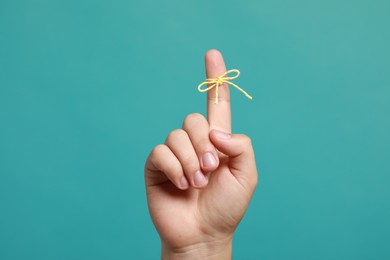 Man showing index finger with tied bow as reminder on turquoise background, closeup
