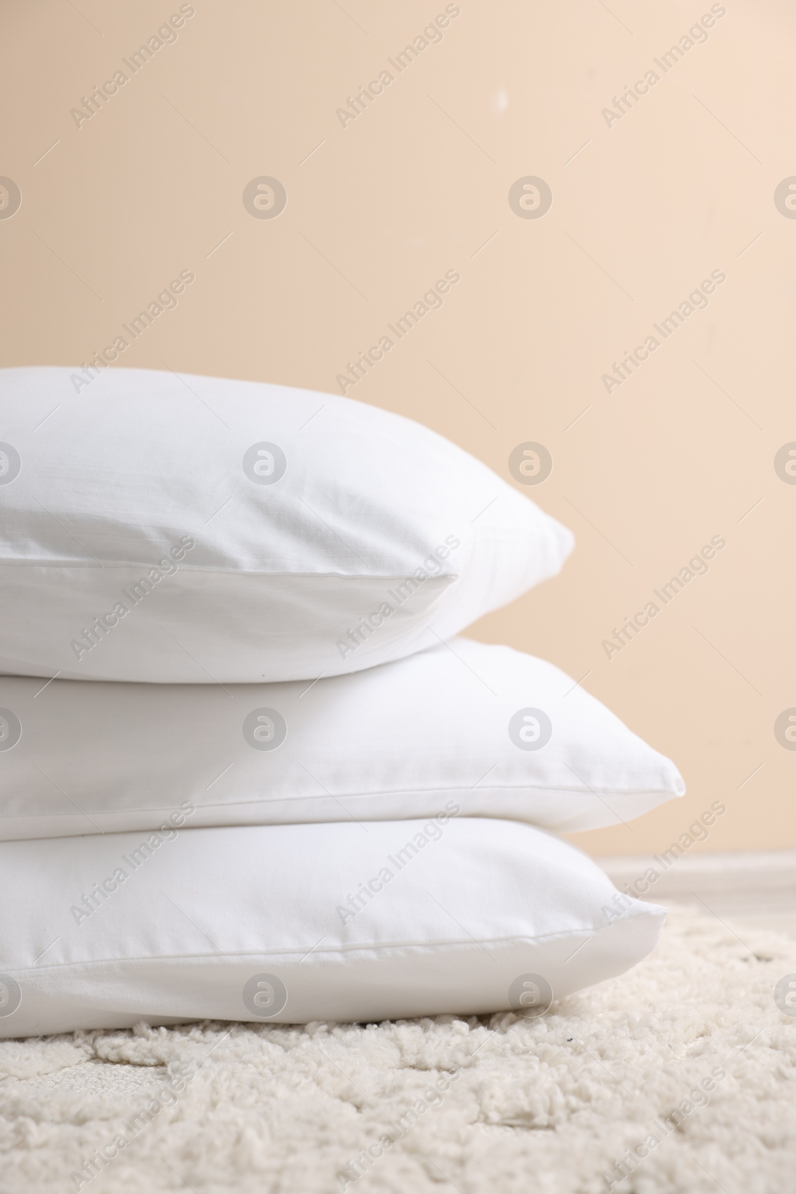 Photo of Stack of soft white pillows near beige wall indoors