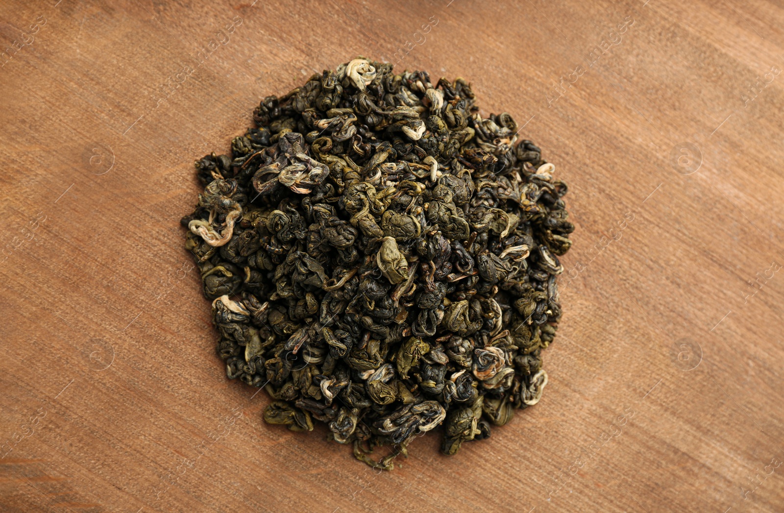 Photo of Heap of dry green tea leaves on wooden table, top view