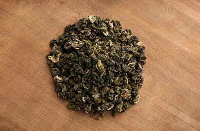 Photo of Heap of dry green tea leaves on wooden table, top view