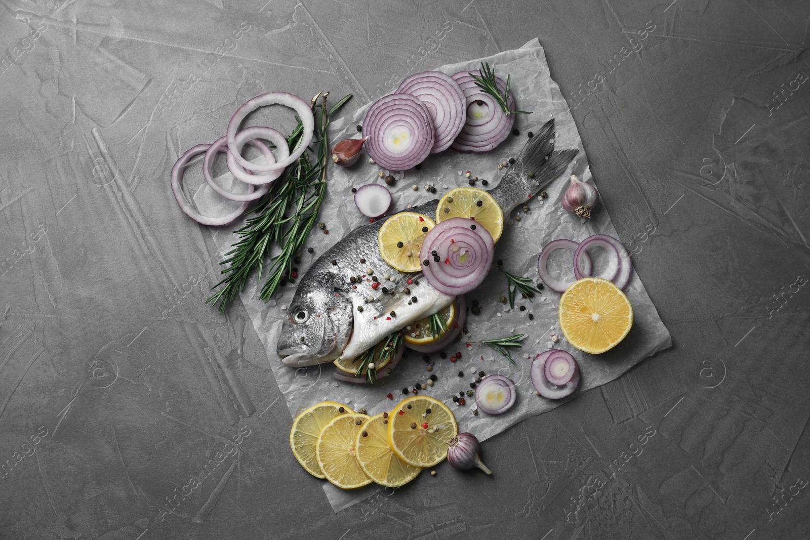 Photo of Raw dorado fish with spices, lemon and onion on grey textured table, top view