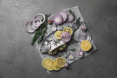 Photo of Raw dorado fish with spices, lemon and onion on grey textured table, top view