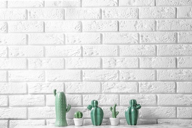 Decorative cacti on table near brick wall, space for text. Interior decor