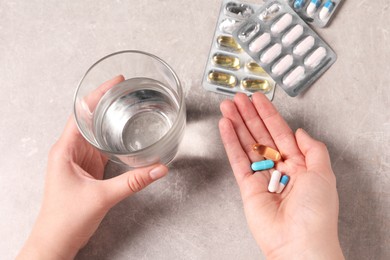 Photo of Woman with different pills and glass of water at grey table, closeup