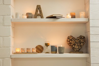 Photo of Burning wax candles and different decor on shelves