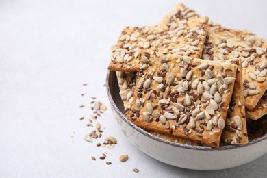 Photo of Cereal crackers with flax, sunflower and sesame seeds in bowl on light textured table, closeup. Space for text
