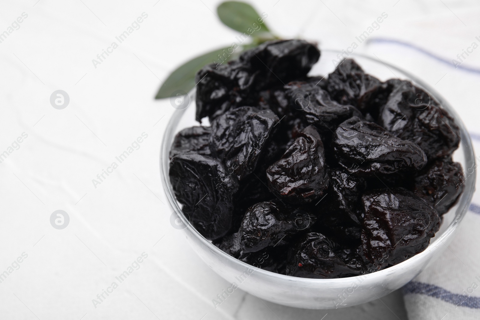 Photo of Sweet dried prunes in bowl on white table, closeup. Space for text