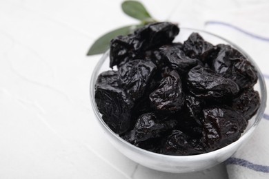 Sweet dried prunes in bowl on white table, closeup. Space for text