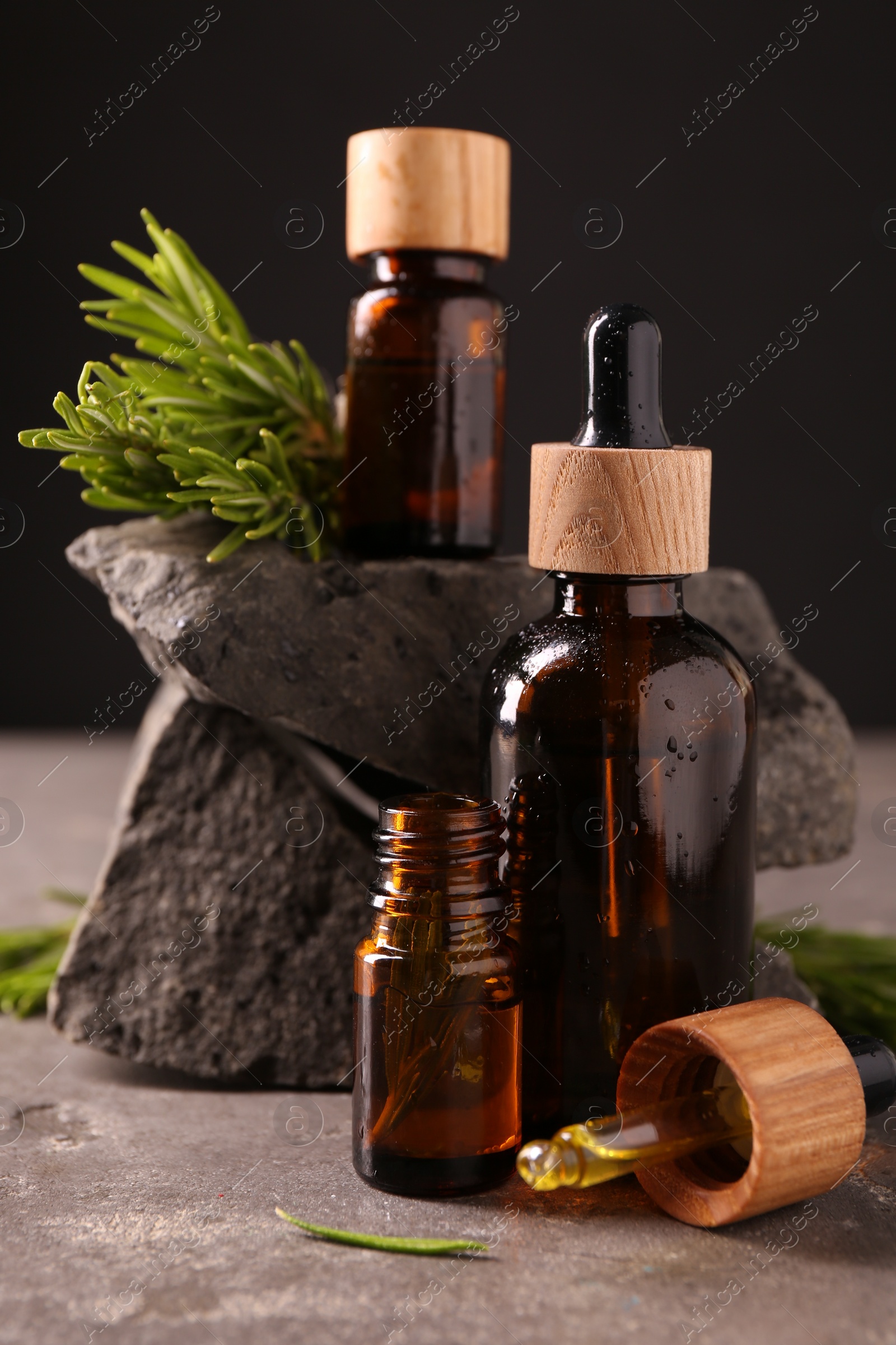 Photo of Essential oil in bottles, dropper and rosemary on grey table