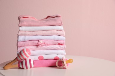 Photo of Stack of clean girl's clothes, pacifier and rattles on table. Space for text