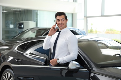 Young man talking on phone near car in modern dealership