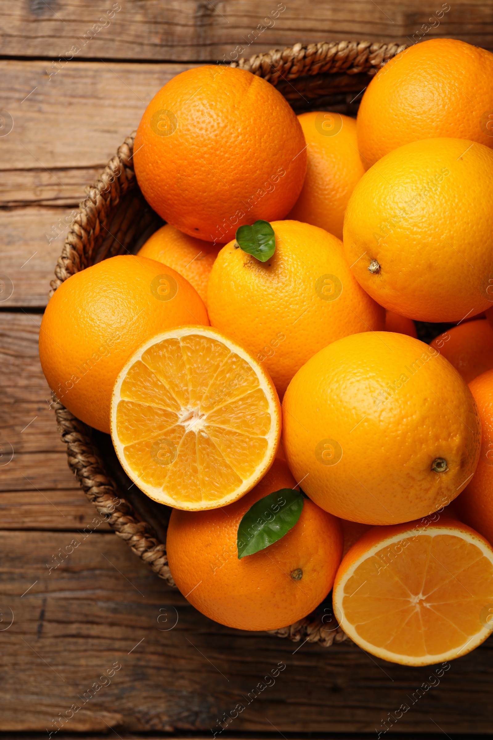 Photo of Many ripe oranges and green leaves on wooden table, top view