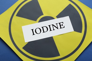 Paper note with word Iodine and radiation sign on blue background, closeup