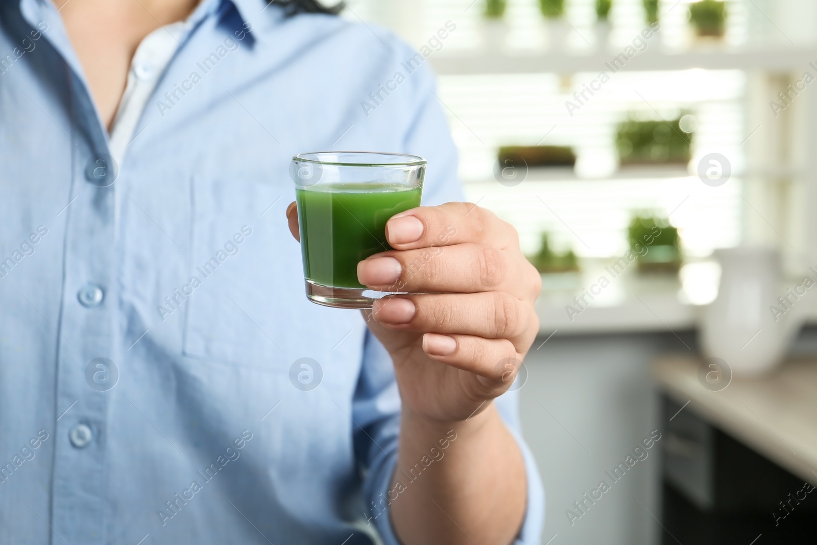 Woman holding shot glass of wheat grass juice indoors, closeup Photo of Woman holding shot glass of wheat grass juice indoors, closeup
