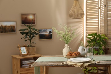 Photo of Clean tableware, flowers and fresh pastries on table in stylish dining room