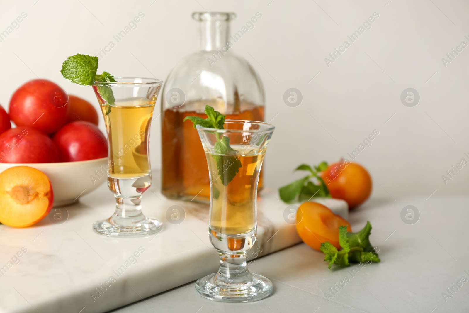 Photo of Delicious plum liquor with mint and ripe fruits on light table. Homemade strong alcoholic beverage